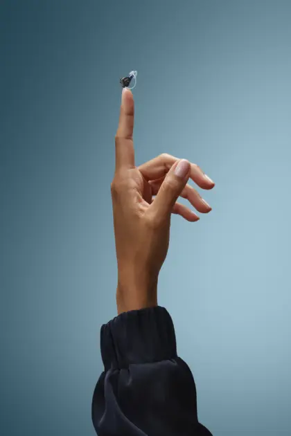 Oticon Zeal Product on Finger Steel blue Background KC 25 2 4848 Vertical